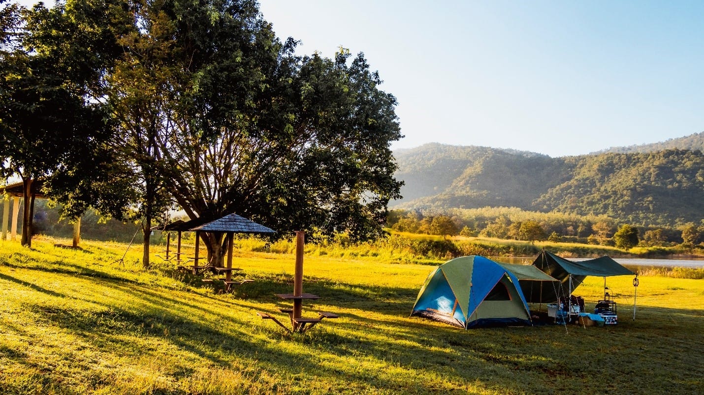 A campsite on grass field-by trees-mountain view-sunny day