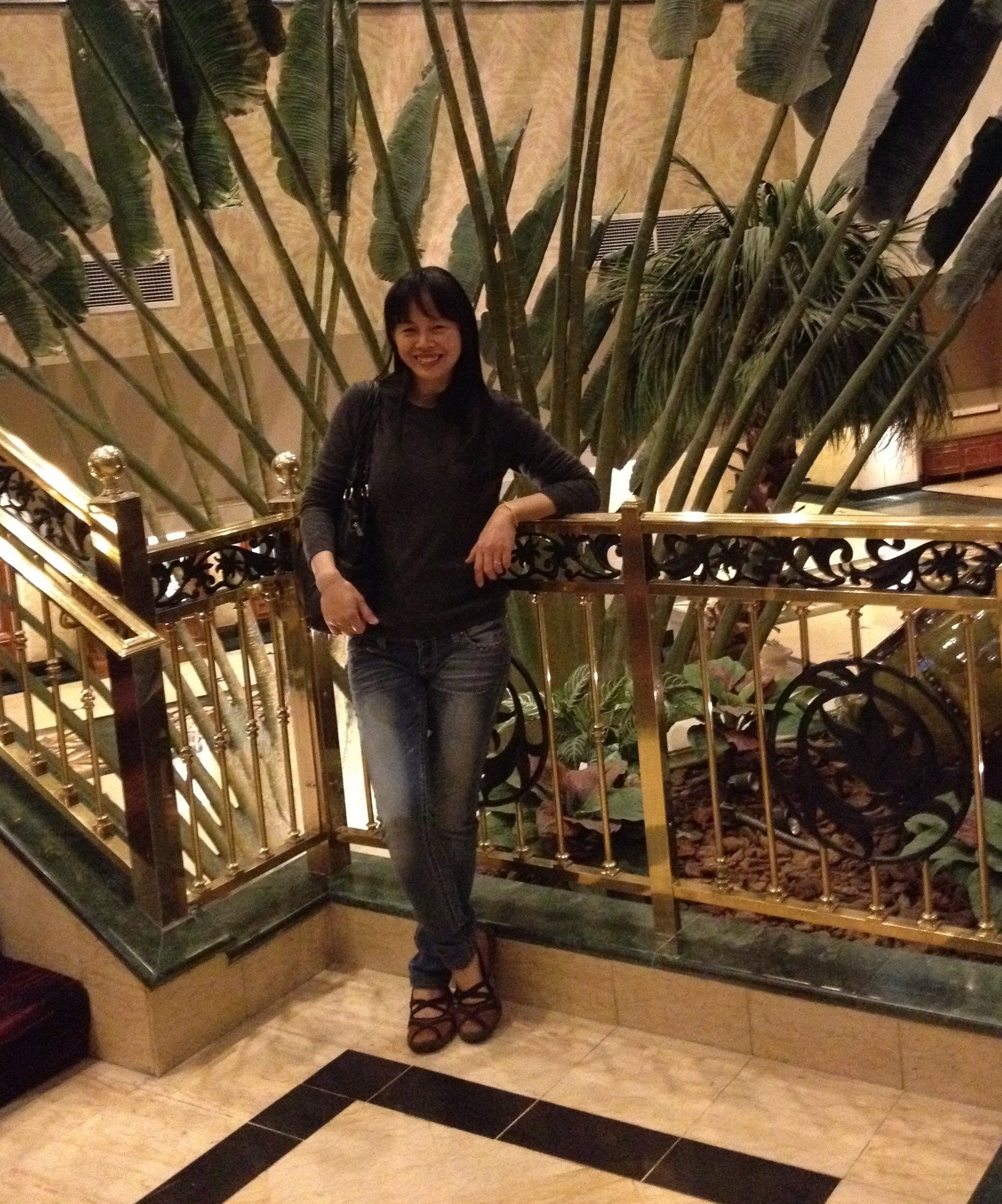 A picture of me standing by the rails on a 2nd floor of a hotel with banana leaves background.