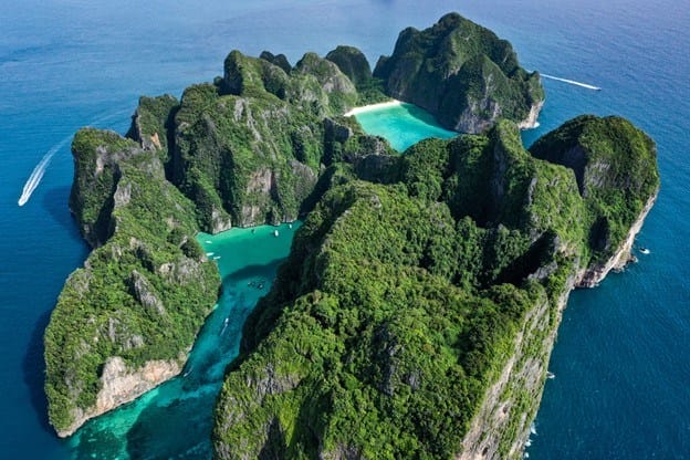 paranomic view of Maya Bay in Phi Phi Leh Island with dark green cliffs around turquois bays, and surrounded by the boats on the blue ocean