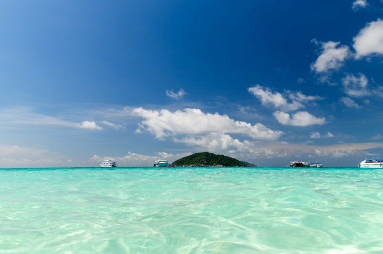 Similan Islands view from far away with clear light green ocean and a few boats nearby