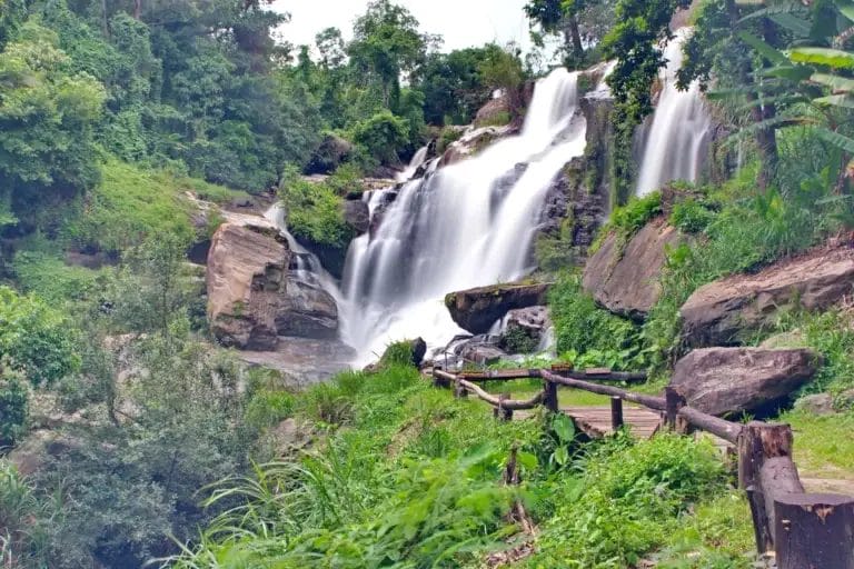 Giant waterfall with big rocks and wooden path with rails.