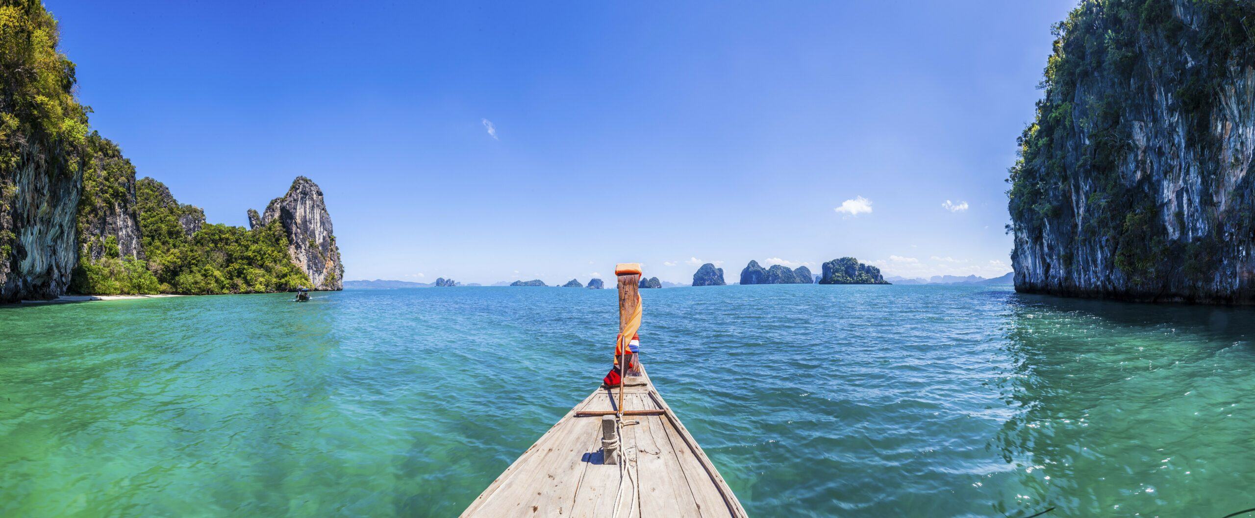 A long tail boat in the green ocean in Phang Nga Bay with islands and blue sky